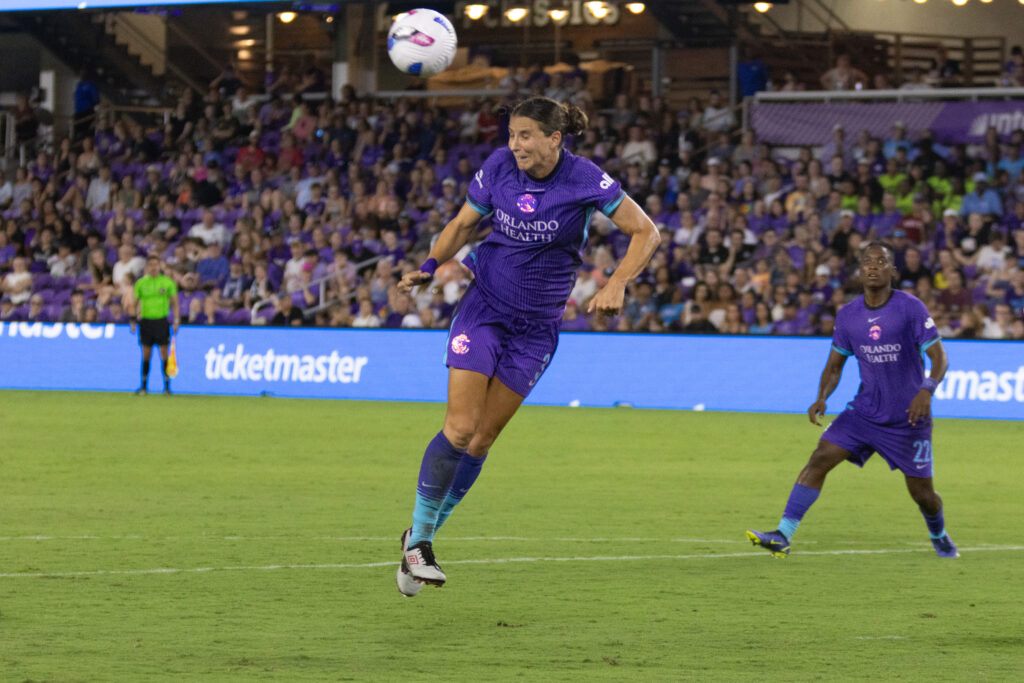 Image of Kylie Nadaner making a headed clearance against the Houston Dash while Barbra Banda looks on.
