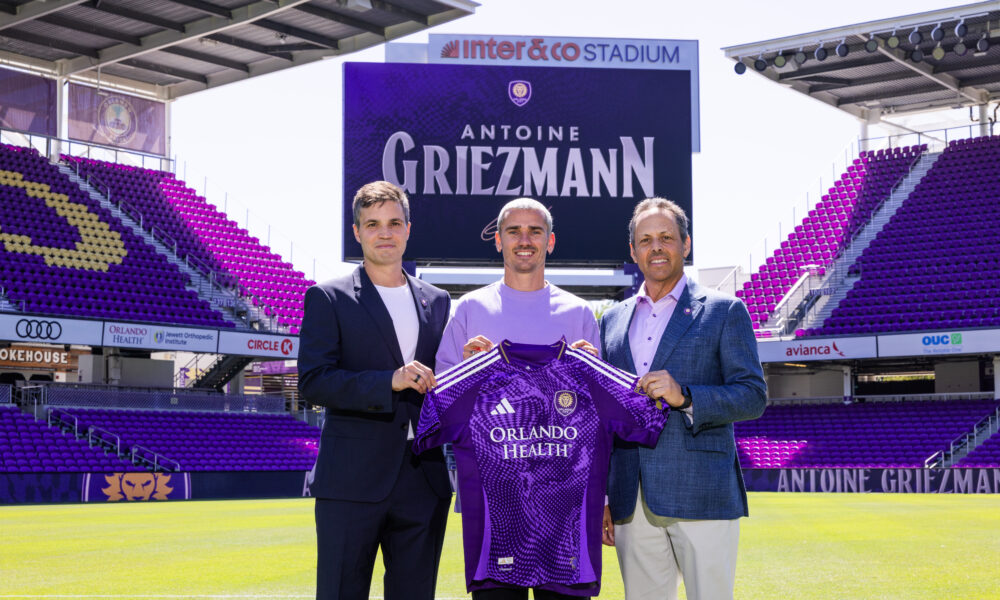 Image of Antoine Griezmann posing with his Orlando City kit alongside Ricardo Moreira and Mark Wilf.