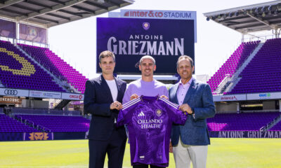 Image of Antoine Griezmann posing with his Orlando City kit alongside Ricardo Moreira and Mark Wilf.