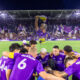 Image of Orlando City players huddled together with a tifo displayed in the background.