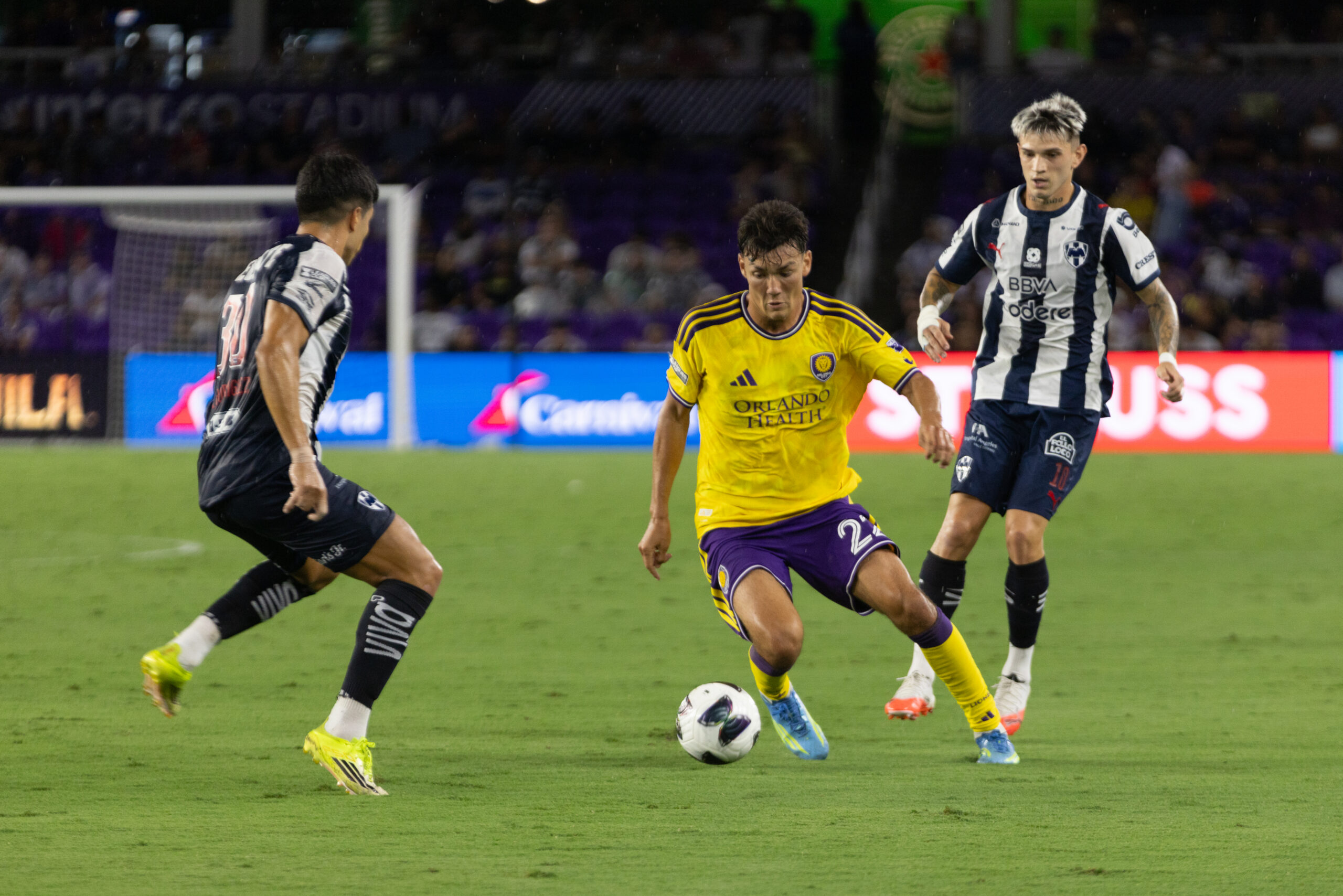 Image of Justin Ellis dribbling the ball between two Monterrey defenders.